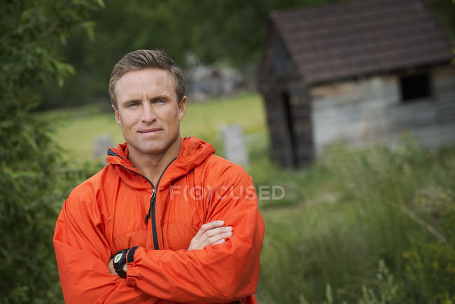 Metà uomo adulto con le braccia piegate in giacca arancione brillante in posa in campagna . — Foto stock