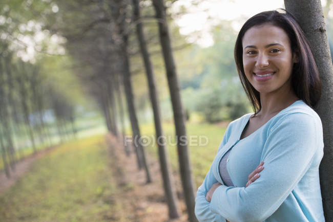 Young woman with arms folded leaning against tree in country. — Stock Photo