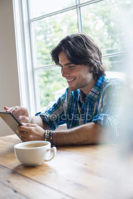 Молодий чоловік використовує цифровий планшет, сидячи в кафе з чашкою кави . — стокове фото
