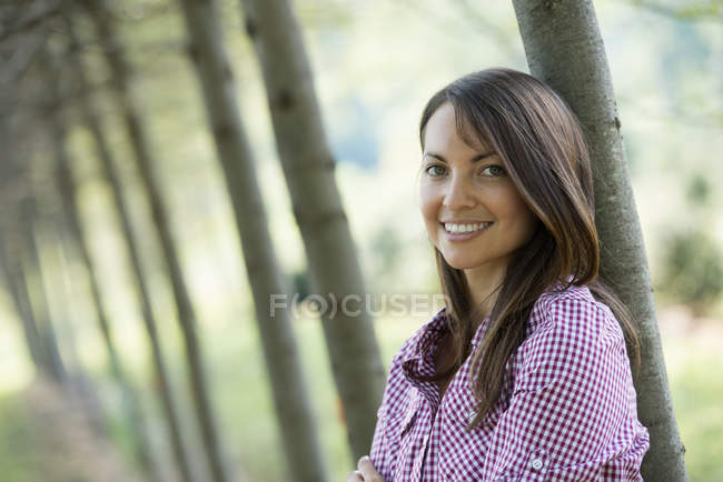 Frau steht in Baumallee und lächelt. — Stockfoto