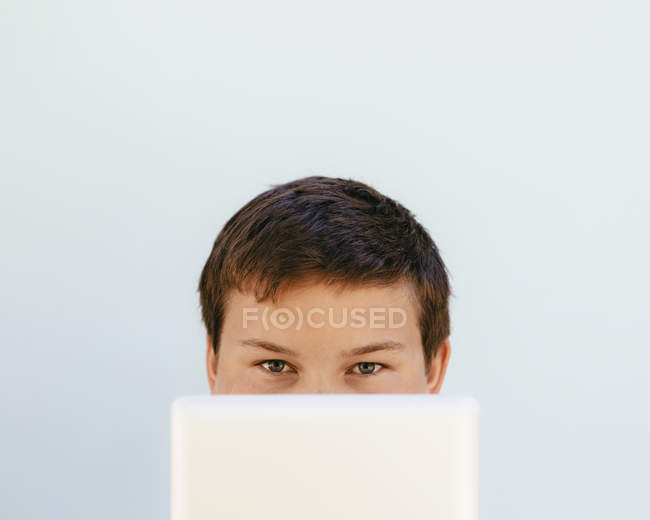 Portrait of pre-adolescent boy hiding face behind digital tablet. — Stock Photo