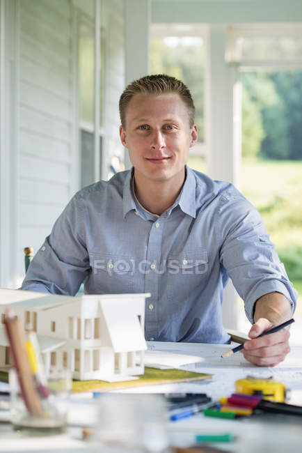Mitte erwachsener Mann arbeitet an Modell eines Bauernhauses am Tisch auf dem Land. — Stockfoto