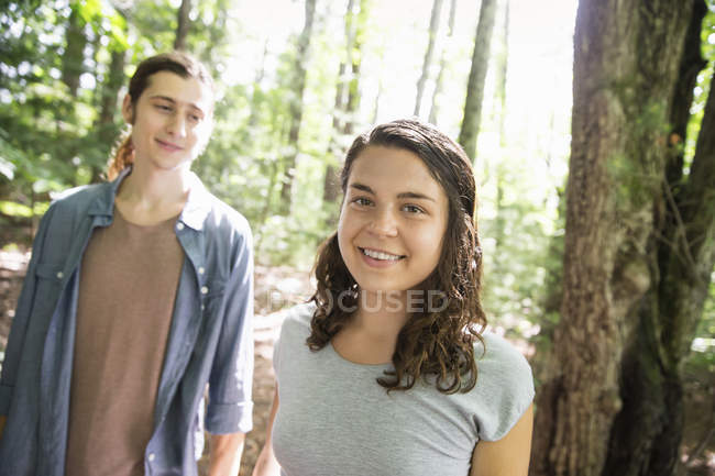 Young woman and man standing side by side in sunny woods. — Stock Photo