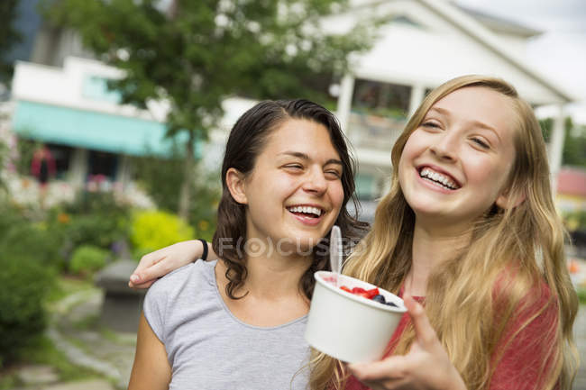 Teen girls hugging, laughing and holding bowl of ice cream — Stock Photo
