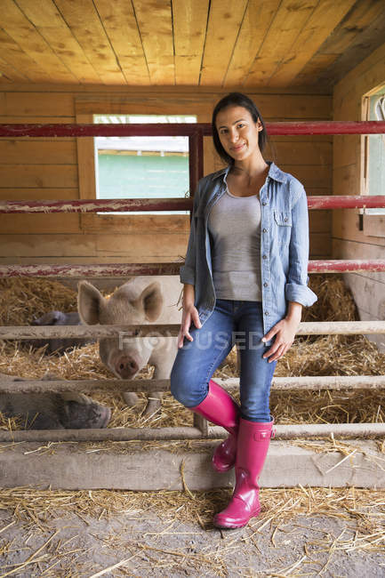 Frau steht auf Bauernhof neben Schweinen im Stall. — Stockfoto