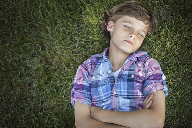 Vista aérea del niño con los brazos cruzados acostado sobre hierba verde con los ojos cerrados . - foto de stock