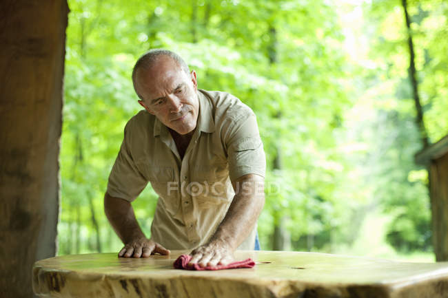 Mature man polishing outdoor wooden furniture in countryside — Stock Photo