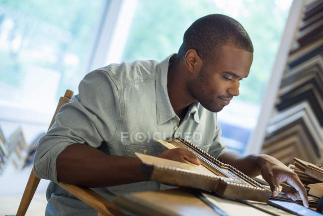 Giovane uomo che tiene cornice e utilizzando tablet digitale al banco da lavoro in studio di inquadratura . — Foto stock