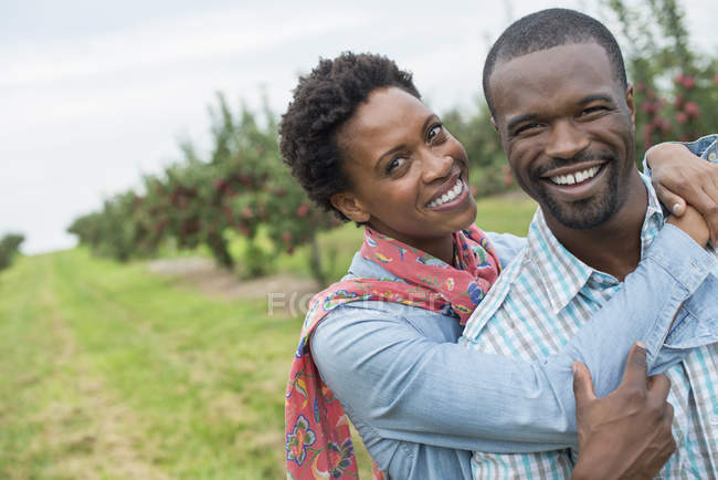 Пара обіймає і посміхається в камері в органічному яблуневому саду . — стокове фото