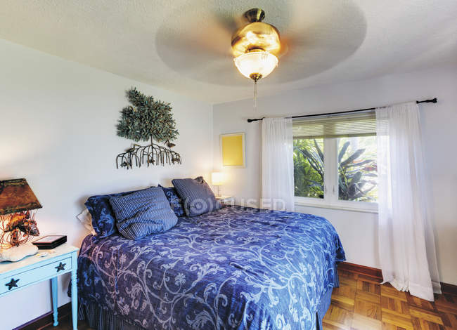 Кровать с огнеупорным дизайном, синяя подстилка, потолочный вентилятор и окно — стоковое фото