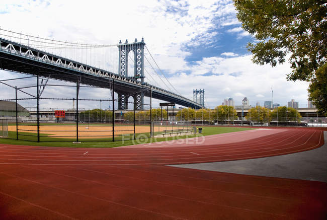 Ciudad campo de deportes con pistas, paisaje urbano y puente urbano, Nueva York, EE.UU. - foto de stock