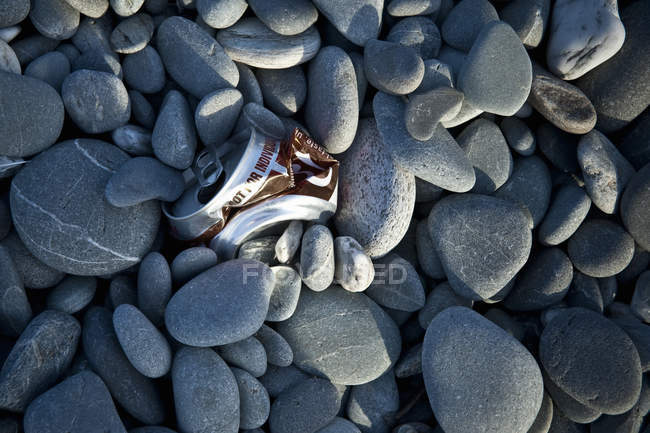 Primer plano de la lata triturada en rocas de guijarros, Coopers Beach, Isla Norte, Nueva Zelanda - foto de stock