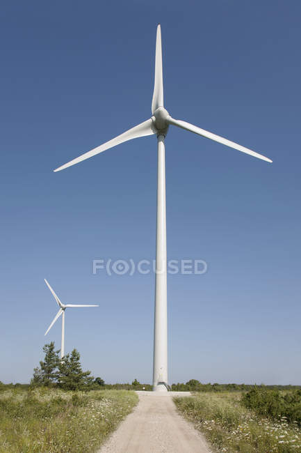 Turbines éoliennes tournantes par route de terre rurale — Photo de stock