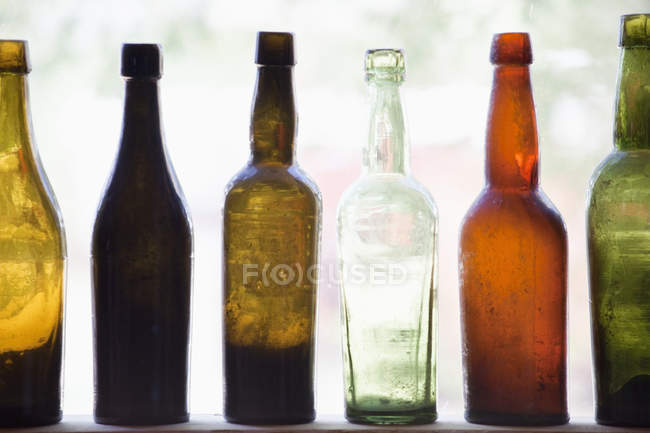 Антикварные бутылки, сложенные в ряд на полке за окном — стоковое фото