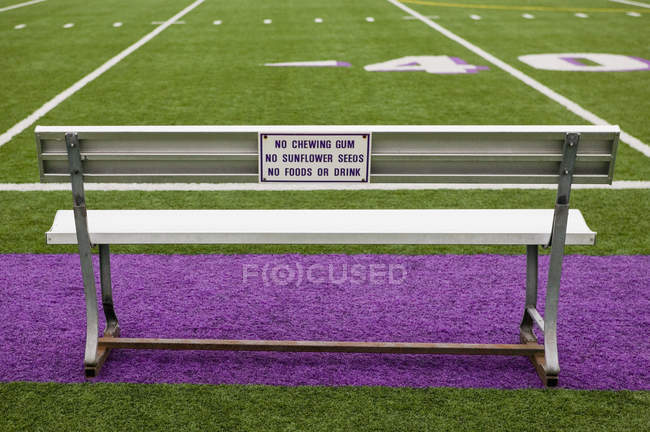 Signos en el banco del campo de atletismo con hierba verde y púrpura - foto de stock