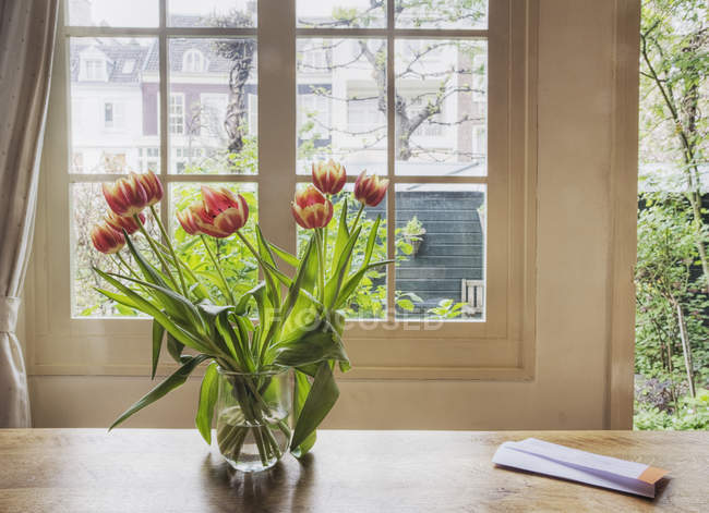 Tulips in vase on table by house window — Stock Photo