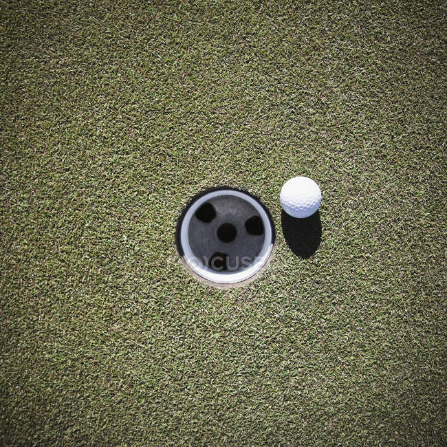 Primer plano de la pelota de golf junto a la taza de poner - foto de stock
