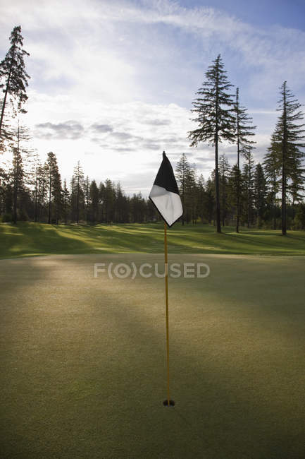 Golf mettant vert au coucher du soleil avec drapeau sur le poteau — Photo de stock