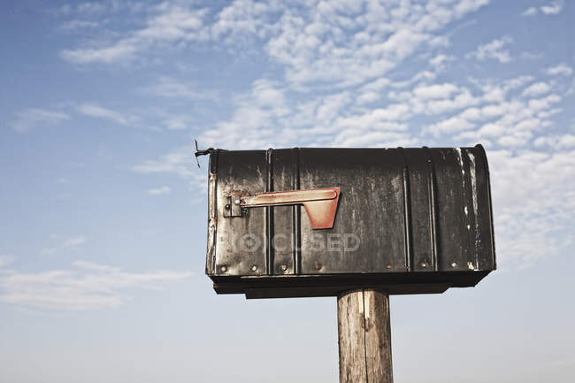 Cassetta postale su palo di legno contro cielo nuvoloso — Foto stock