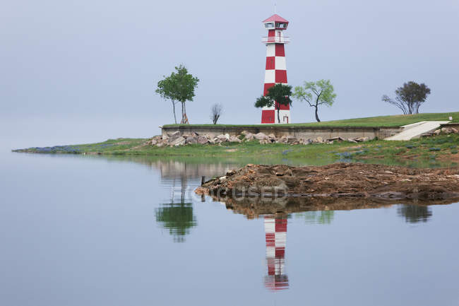 Leuchtturm am grünen Strand mit Spiegelung im Wasser — Stockfoto