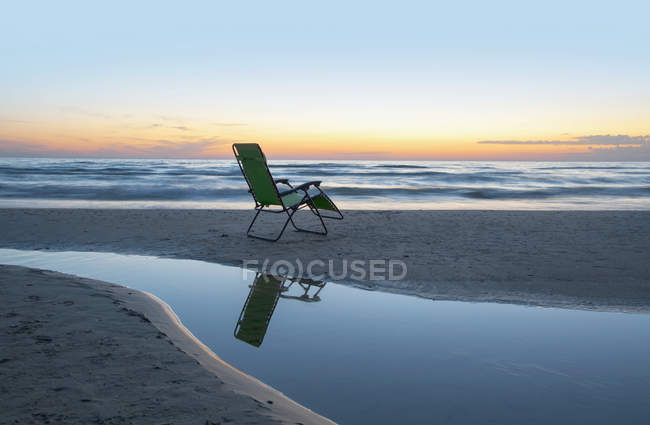 Lounge chair on beach at sunset with reflection in water, Canada — Stock Photo