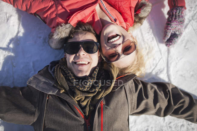 Young couple in sunglasses smiling while lying in snow in winter — Stock Photo