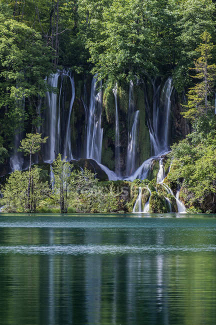 Cachoeira derramando sobre formações rochosas para lago remoto — Fotografia de Stock