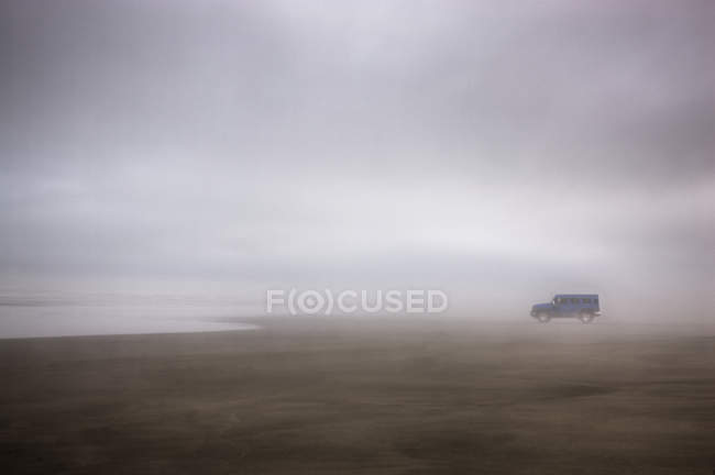 Грузовик припаркован на мокром песке на туманном пляже в штормовую погоду — стоковое фото