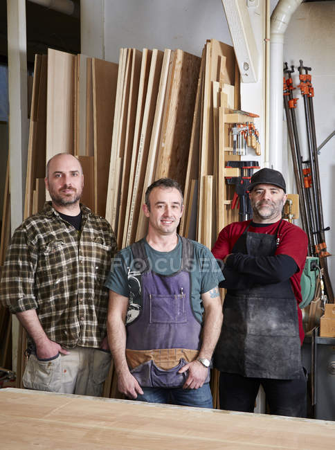Плотники-мужчины улыбаются, стоя в интерьере мастерской — стоковое фото