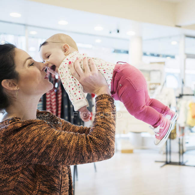 Mãe branca levantando bebê filha enquanto faz compras na loja — Fotografia de Stock