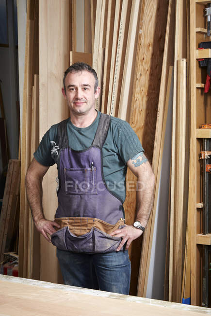 Carpintero de pie y sonriendo en el interior del taller - foto de stock