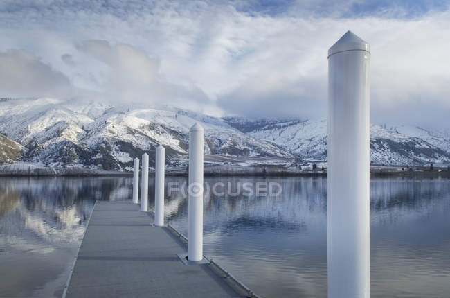 Pilastri sul molo al lago vicino alla catena montuosa innevata — Foto stock