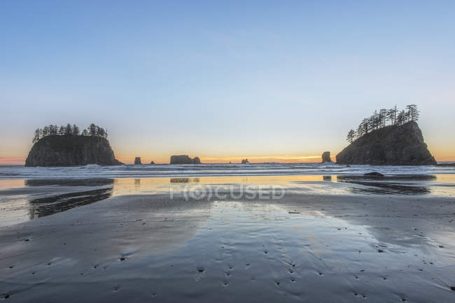 Sunrise horizon behind rock formation on scenic beach — Stock Photo