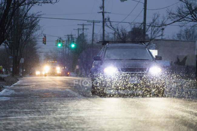 Cars driving on snowy urban street in wet weather at night — Stock Photo