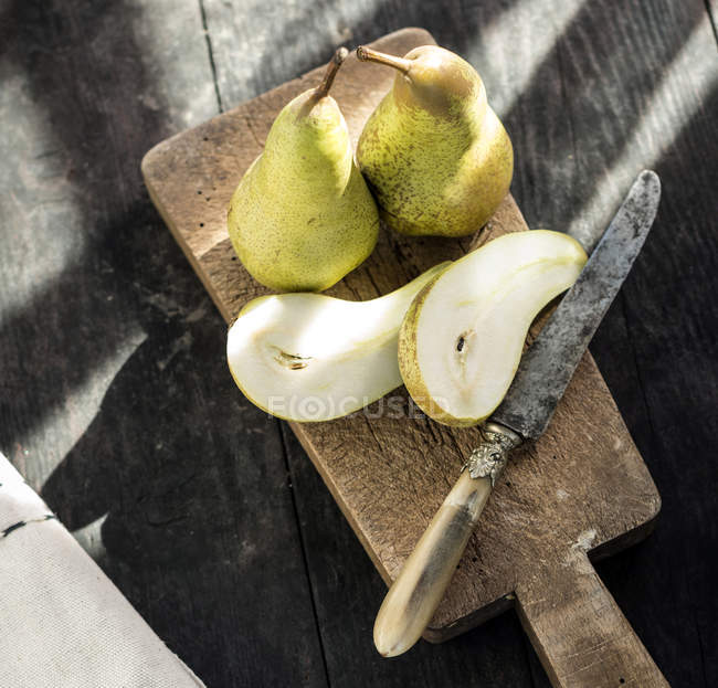 Primer plano de peras frescas en rodajas sobre tabla de madera con cuchillo vintage, vista superior - foto de stock