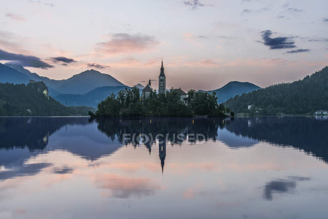 Aldeia igreja e edifícios refletidos em lago imóvel, Bled, Upper Carniola, Eslovênia — Fotografia de Stock