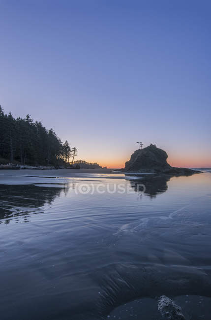 Amanecer horizonte detrás de la formación de rocas en la playa - foto de stock