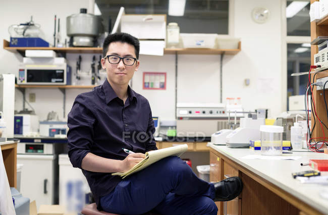 Uomo asiatico che scrive su blocco note in laboratorio di elettronica . — Foto stock