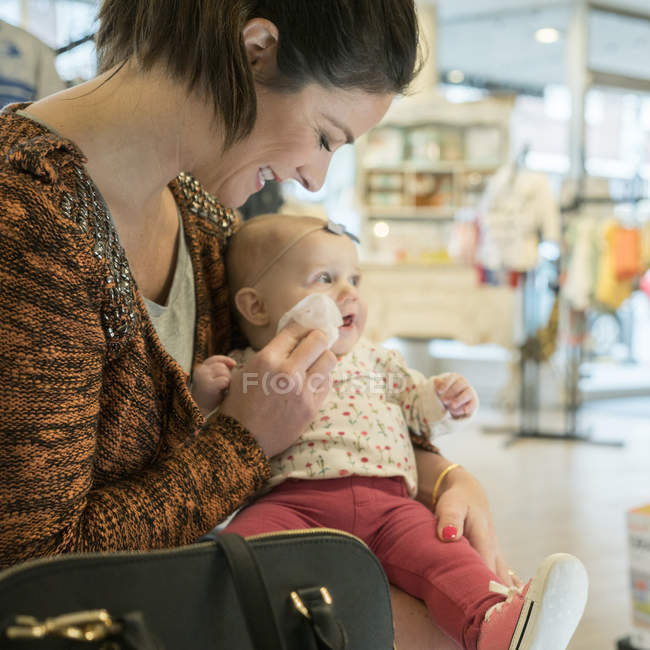 Caucasian mother wiping cheeks of baby daughter in store — Stock Photo