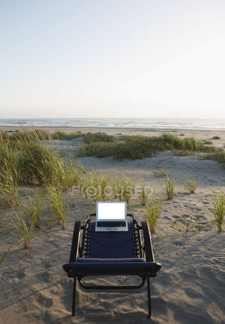 Laptop on deck chair overlooking grassy beach — Stock Photo