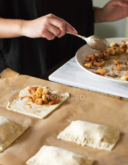 Baker filling miniature apple pies by table, close-up — Stock Photo