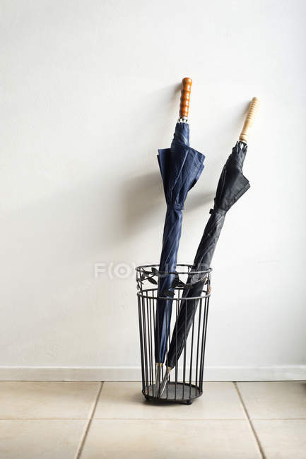 Two umbrellas in wire stand on floor indoors. — Stock Photo