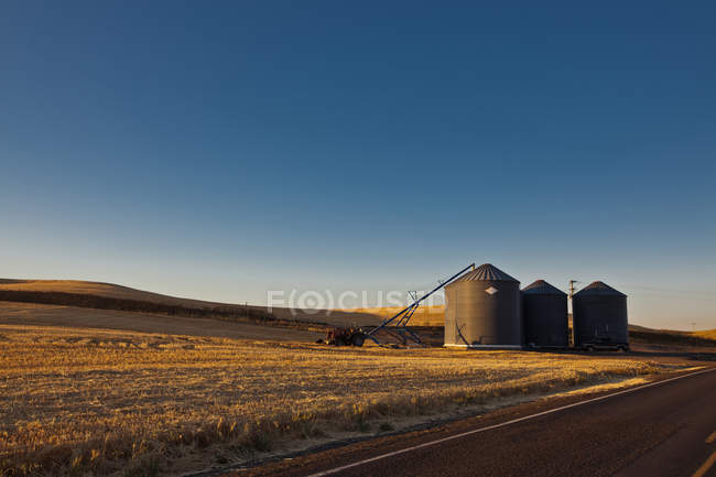 Silos le long de la route rurale sous le ciel bleu au coucher du soleil dans le pays — Photo de stock