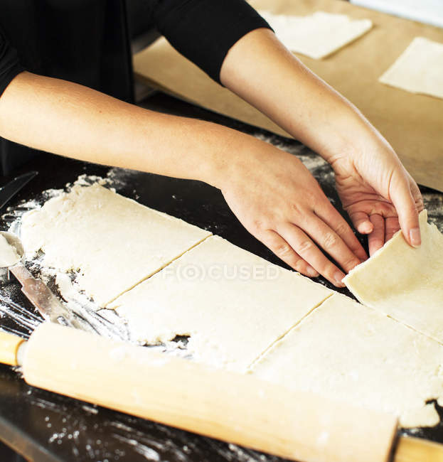 Mani di donna panettiere taglio pasta torta in quadrati — Foto stock
