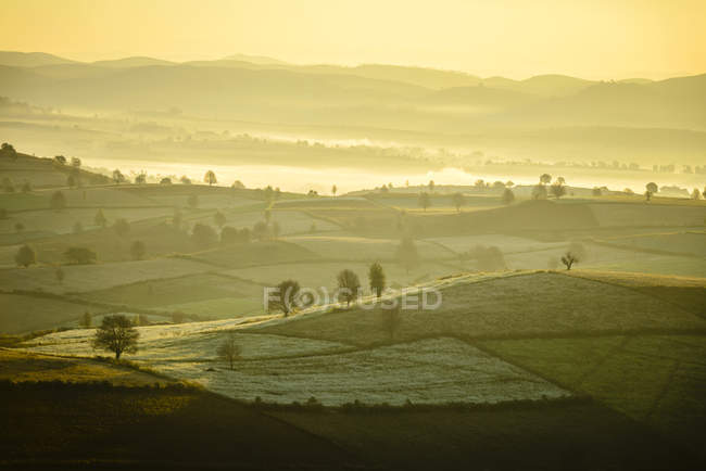 Salida del sol sobre tierras de cultivo en el paisaje rural - foto de stock