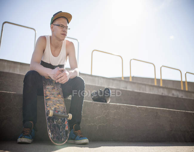 Белый мужчина со скейтбордом сидит на ступеньках — стоковое фото