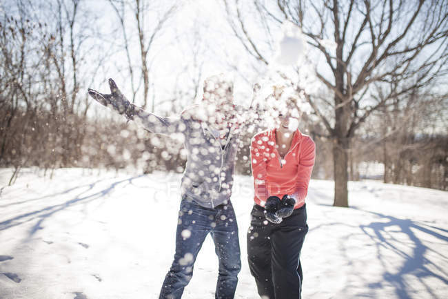 Pareja joven lanzando bolas de nieve en el parque de invierno - foto de stock