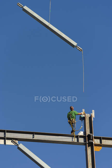 Vista de bajo ángulo del trabajador de la construcción en andamios contra el cielo azul, Seattle, Washington, EE.UU. - foto de stock