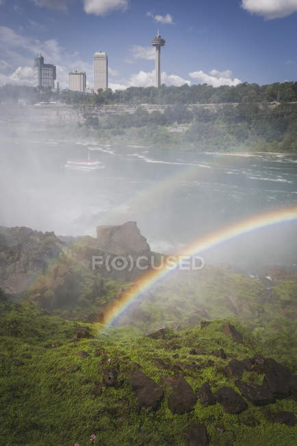 Doble arco iris sobre el río por las Cataratas del Niágara con edificios en la distancia, Nueva York, Estados Unidos - foto de stock