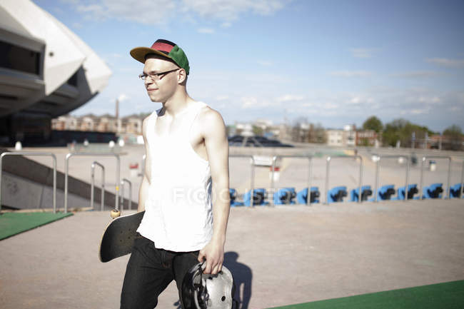 Caucasian man carrying skateboard near stadium — Stock Photo